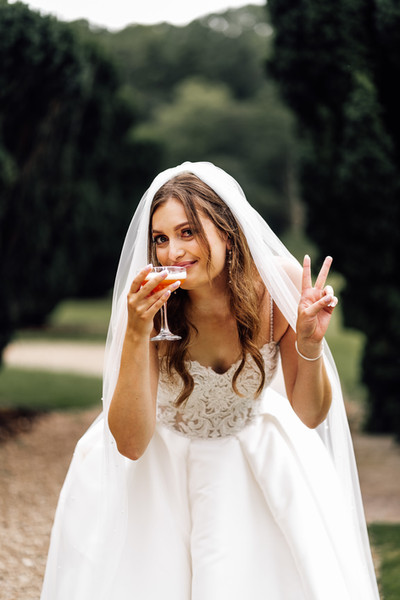 Bride drinking a cocktail in a beautiful veil with her fingers showing the victory sign