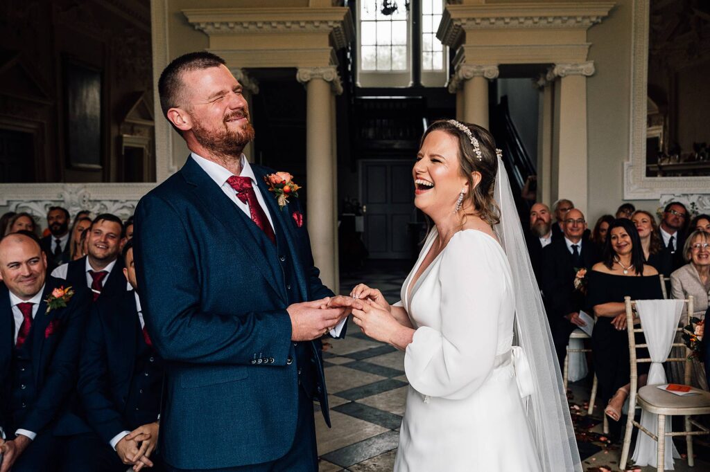 Bride laughs whilst groom grimaces during the exchange of rings