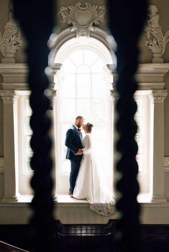 Groom kisses bride whilst stood in a large window