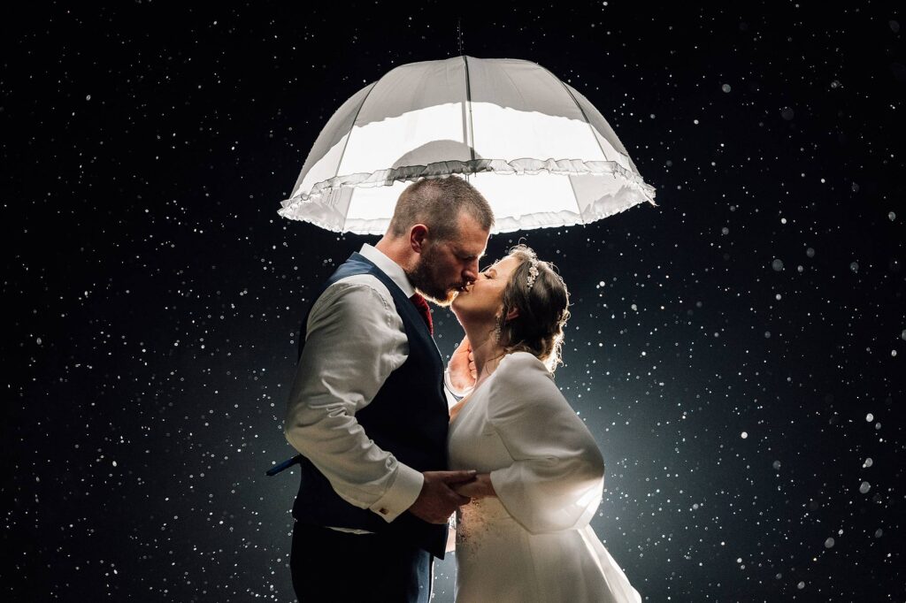 A rainy umbrella photo of bride & groom kissing